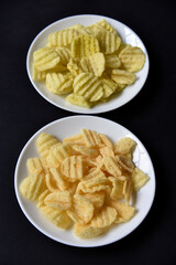 Delicious peppery corn chips on a white plate. Beer appetizer on a plate on a black background.