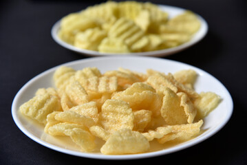 Delicious peppery corn chips on a white plate. Beer appetizer on a plate on a black background.