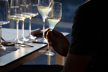 A right hand holds a crystal glass with white wine against the light