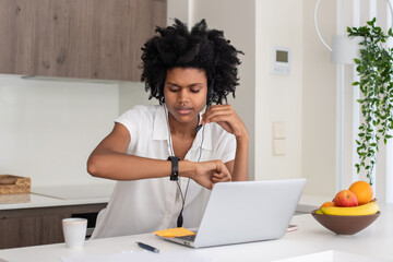 Woman watching time on wristwatch during online conference. Young busy businesswoman talking with colleagues using laptop, working from home. Home office, communication, connection concept