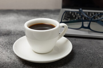 Top view of the office desk. Workspace with laptop, glasses and coffee cup on textural black background.Flat lay.