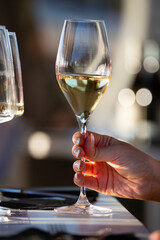A right hand holds a crystal glass with white wine