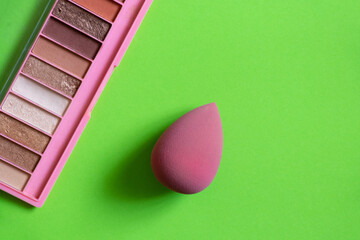 Pink sponge and multi-colored shadows lie on a green background, beauty and makeup, cosmetics