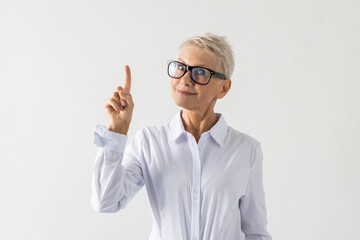 Portrait of senior woman pointing up. Female model in white shirt having idea, smiling. Portrait, studio shot, creativeness concept