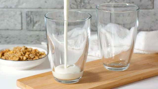 Pouring homemade kefir, buttermilk or yogurt with probiotics. Yogurt flowing from glass bottle on light background. Probiotic cold fermented dairy drink. Trendy food and drink