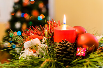 Candle with Christmas objects around and next to two glasses of champagne and a Christmas tree in the background.