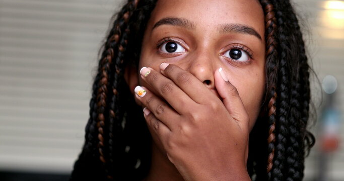 Child shocking reaction to news, black ethnicity girl suprised covering mouth with hand