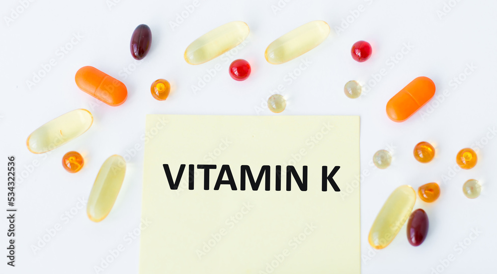 Wall mural Vitamin K text on yellow card on white background next to scattered pills, medical concept - Wall murals