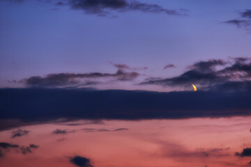 Blue hour with the moon and clouds in the red blue sky. Moon obscured by clouds in the evening light.