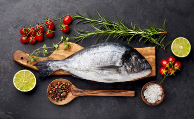 Dorado fish on the black background  with lime, rosemary, tomatoes, pepper  and salt. Top view.