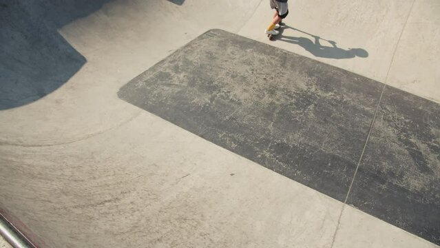 Man making trick on kick scooter in concrete bowl, air extreme in skate park, grab and barspin jump, young skater boy. 