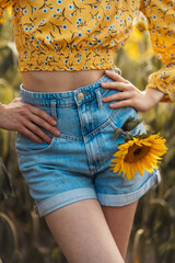 Girl in denim shorts. A sunflower in her pocket. Beginning of autumn. Summer. Concept. Fashion and beauty.