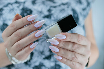 beautiful female hands with long nails light white and blue manicure and a bottle of nail polish