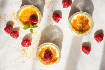 Top view of creme brulee dessert with baked sugar and fresh berries in bright sunshine on linen tablecloth