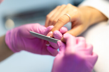 The nail of a young girl or woman in selective focus is cut with a nail file by a manicurist, a manicurist in a beauty salon. Nail care during manicure procedure.