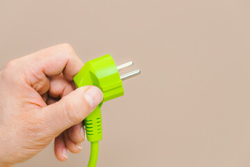 Green plug in hand, Latte-colored background, The concept of using green energy and the use of...