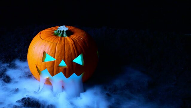 Smoke coiled from the face of a Halloween Pumpkin with different colored lights.