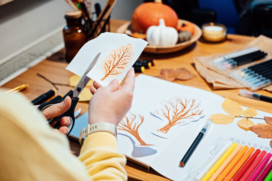 Autumn craft for adults. Faceless portrait of woman drawing autumn trees with markers and cutting out collage from paper.