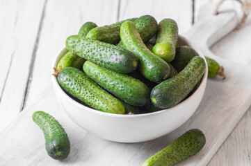 Fresh ripe organic small gherkin cucumbers in bowl on wooden table, not marinated vegetable, cornichon