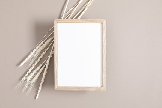 Wooden photo frame mockup with dry plant on beige background. Autumn composition. Flat lay, top view, copy space