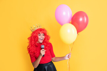 happy kid in crown with microphone and party balloon on yellow background