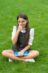 Happy teen school girl adjusting glasses sitting on grass. School and education. Back to school