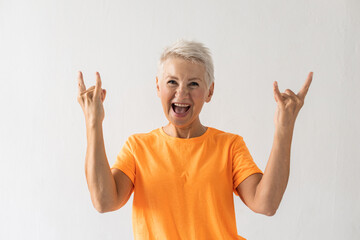 Portrait of senior woman showing rock sign. Female model in orange T-shirt making rock gesture and...