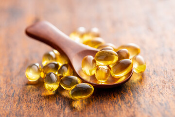 Fish oil capsules in spoon. Yellow omega 3 pills on wooden table.
