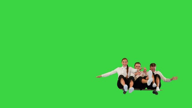 A group of carefree ladies in white shirts and black capri pants have fun riding a skateboard all together on a Green Screen, Chroma Key.