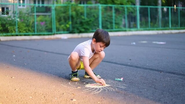 The boy draws with crayons on the asphalt . Children 's drawings . Outdoor games.