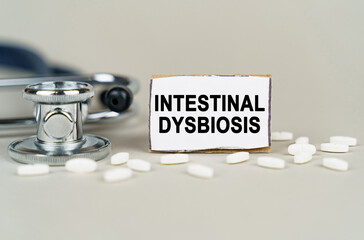 On a gray background, a stethoscope, pills and a cardboard plate with the inscription - Intestinal dysbiosis