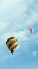 vertical photo two multi-colored balloons fly high in the sky