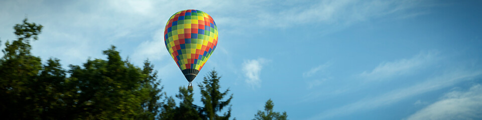 4x1 banner with a flying multi-color balloon against the background of a blue sky with clouds and of a green forest