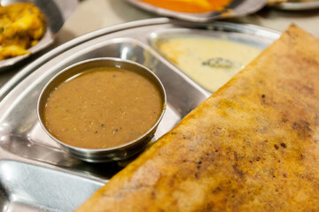 South indian dosa (very thin pancake) with a bowl of dhal (lentil soup) in a typical thali tray, close-up view