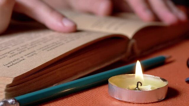 Woman Reading a Book by Candlelight in a Dark Room, Follows a Text with a Finger. Close up. Girl runs finger over old yellow page of an ancient, antique book. Mysterious, mystical atmosphere. Night.