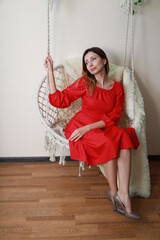 Beautiful woman in a red dress sitting on a hanging wicker chair