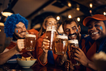 Close up of soccer fans celebrate their team's victory and toast with beer in pub.