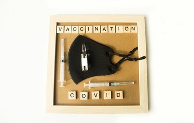 Naklejka premium White isolated background, on the table lies a frame inside her syringe and ampoule, a protective mask, cubes with text. Concept, theme of vaccination and covid 19 renovation. Flat lay, minimalism.