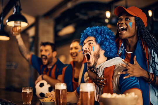 Passionate soccer fans scream while watching game on TV in pub.
