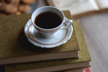 Plate of chocolate chip cookies, stack of vintage books, reading glasses, cup of tea or coffee, lit candle and fairy lights. Hygge at home. Selective focus.