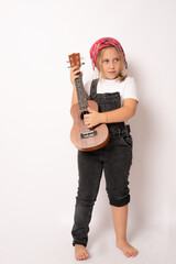 Cute little girl in denim clothing playing ukulele over white background. Happy vacation concept.