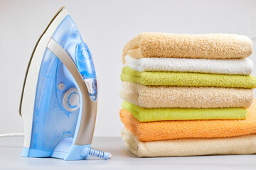Pile of clothes and electric iron on the table on a light background. close-up of ironing tool and towels