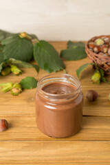 Hazelnut cream with nuts and green leaves on wooden table