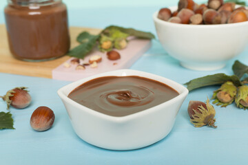 Hazelnut cream with nuts and green leaves on wooden table