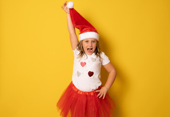Funny cute little girl in red santa hat standing on yellow background. portrait
