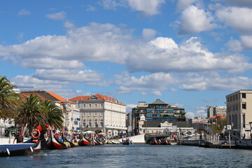 Aveiro, Portugal. 2022 September 25. Traditional boats in the Ria of Aveiro, Portugal.
Colorful Moliceiro boat rides in Aveiro with tourists. Big buildings around the river and colorful bridges.