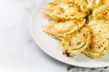 Baked cabbage pieces, roasted cabbage steaks with cheese on white plate and marble background. Vegan diet, healthy food.