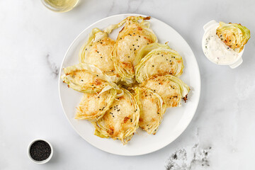 Baked cabbage pieces, roasted cabbage steaks with cheese on white plate and marble background. Vegan diet, healthy food.