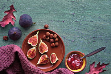 Autumntime background with fresh halved fig fruits on terracotta ceramic plate. Magenta towel and...
