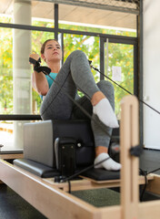 Young woman doing exercises on pilates reformer during training in gym.